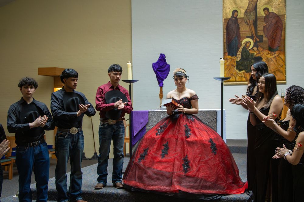 A quinceañera honoree in a red and black ball gown stands at the altar during her church ceremony.