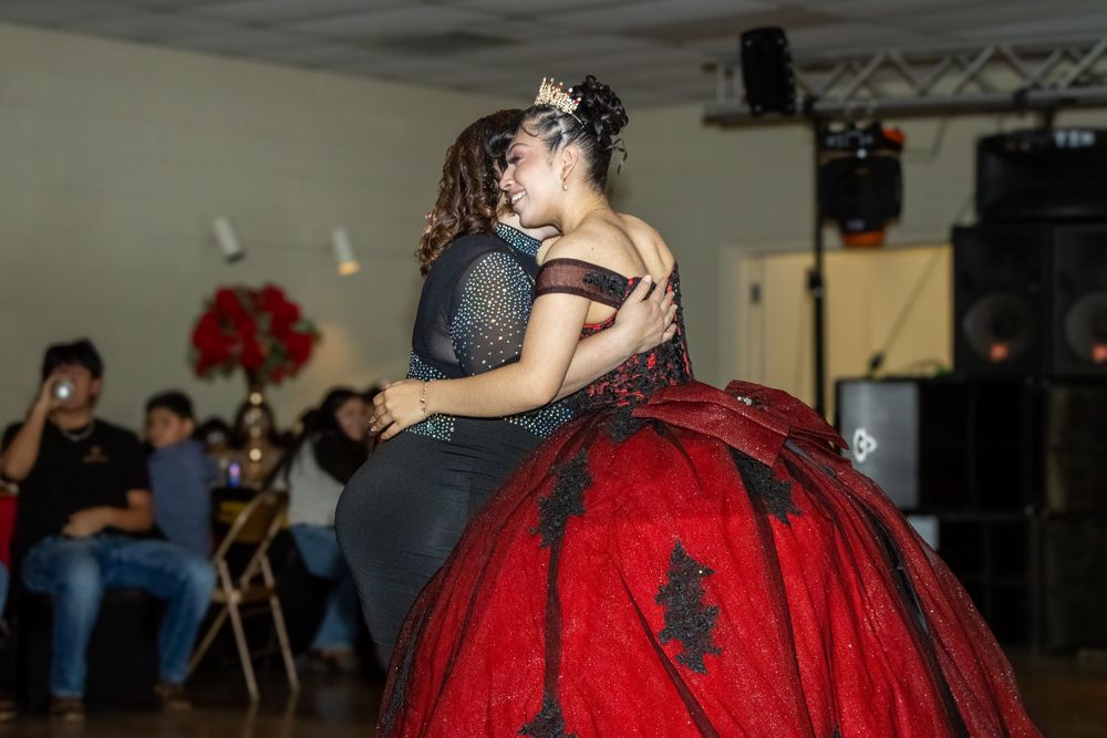 A quinceañera honoree in a red and black ball gown shares a dance with a guest at her reception.