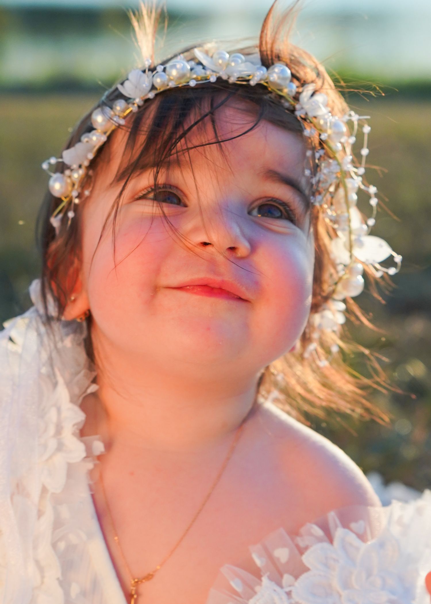 Young child wearing a floral crown gazes upward with a dreamy expression at sunset.