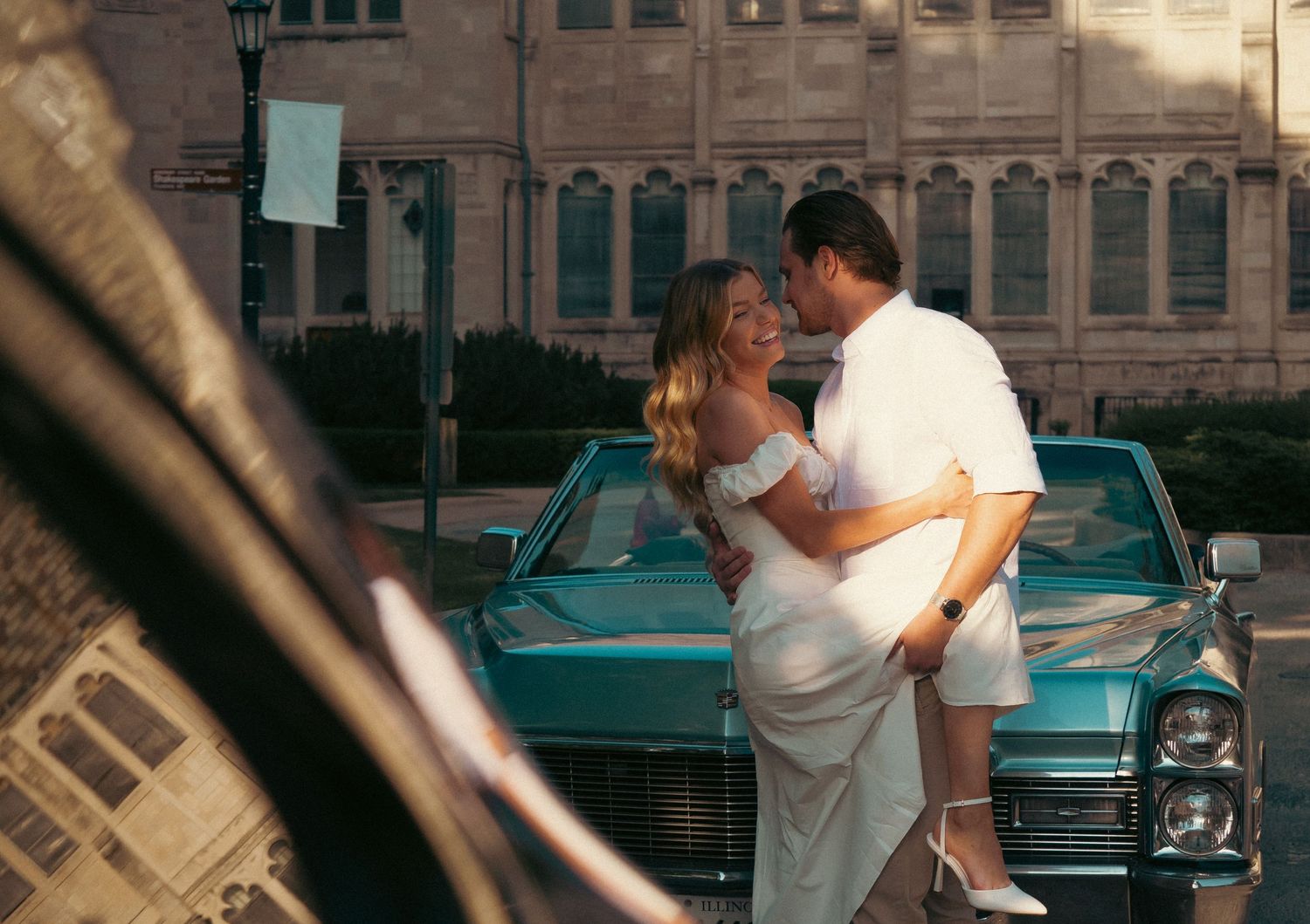 A romantic moment beside a turquoise classic car in front of a historic building.