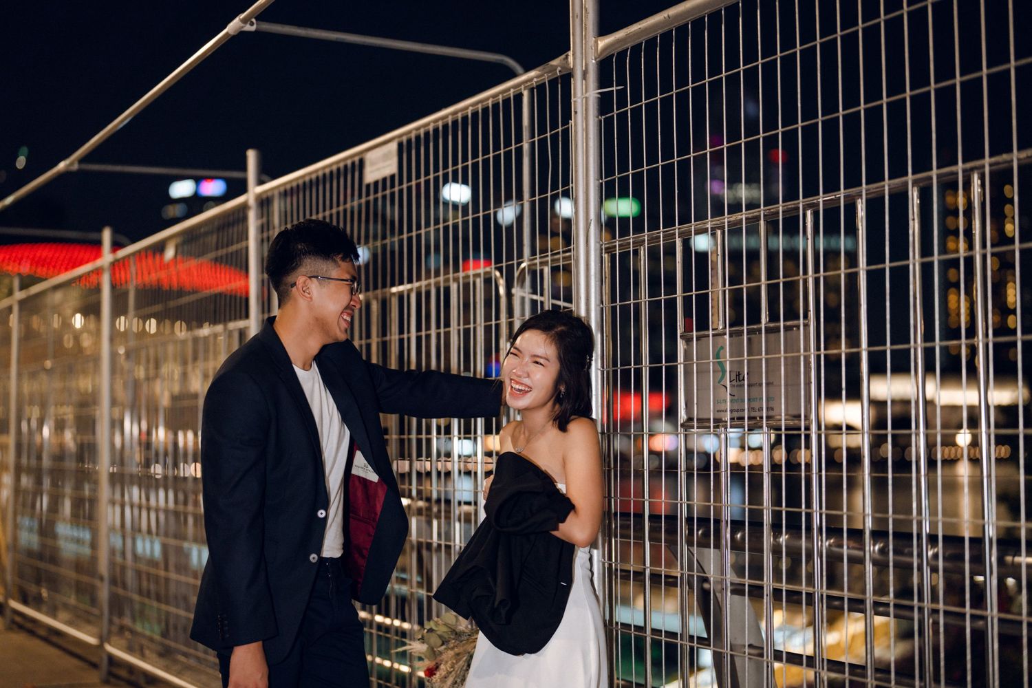 Couple sharing intimate moment along railing at night with urban skyline backdrop.