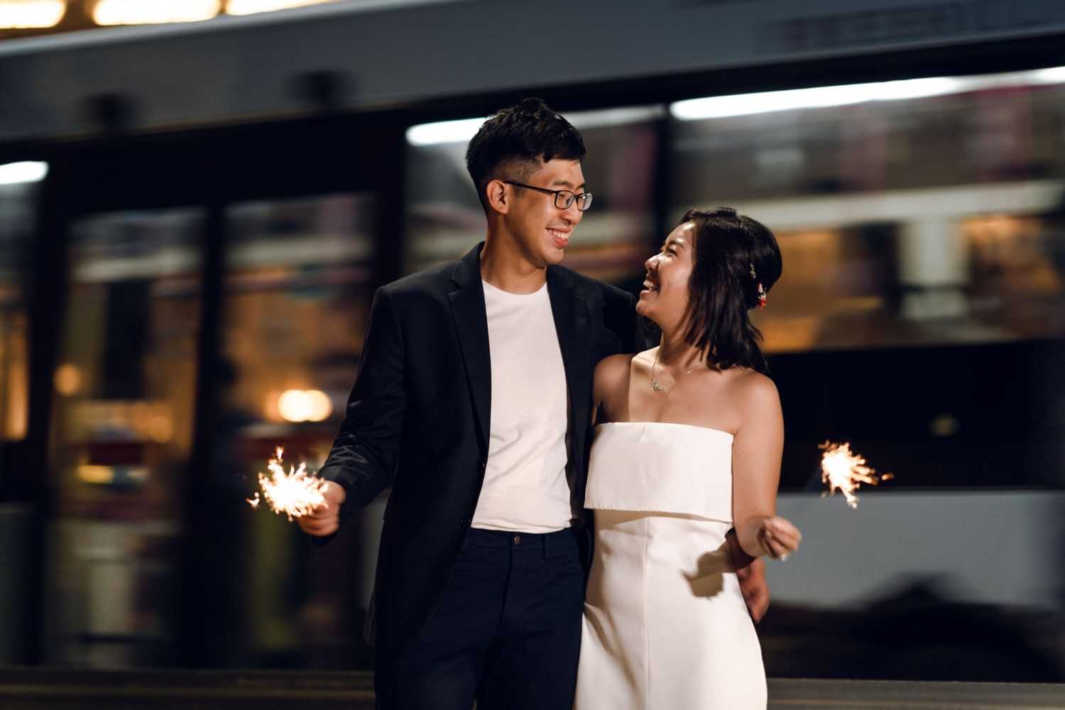 Romantic nighttime couple portrait with sparklers and city lights creating a magical ambiance.