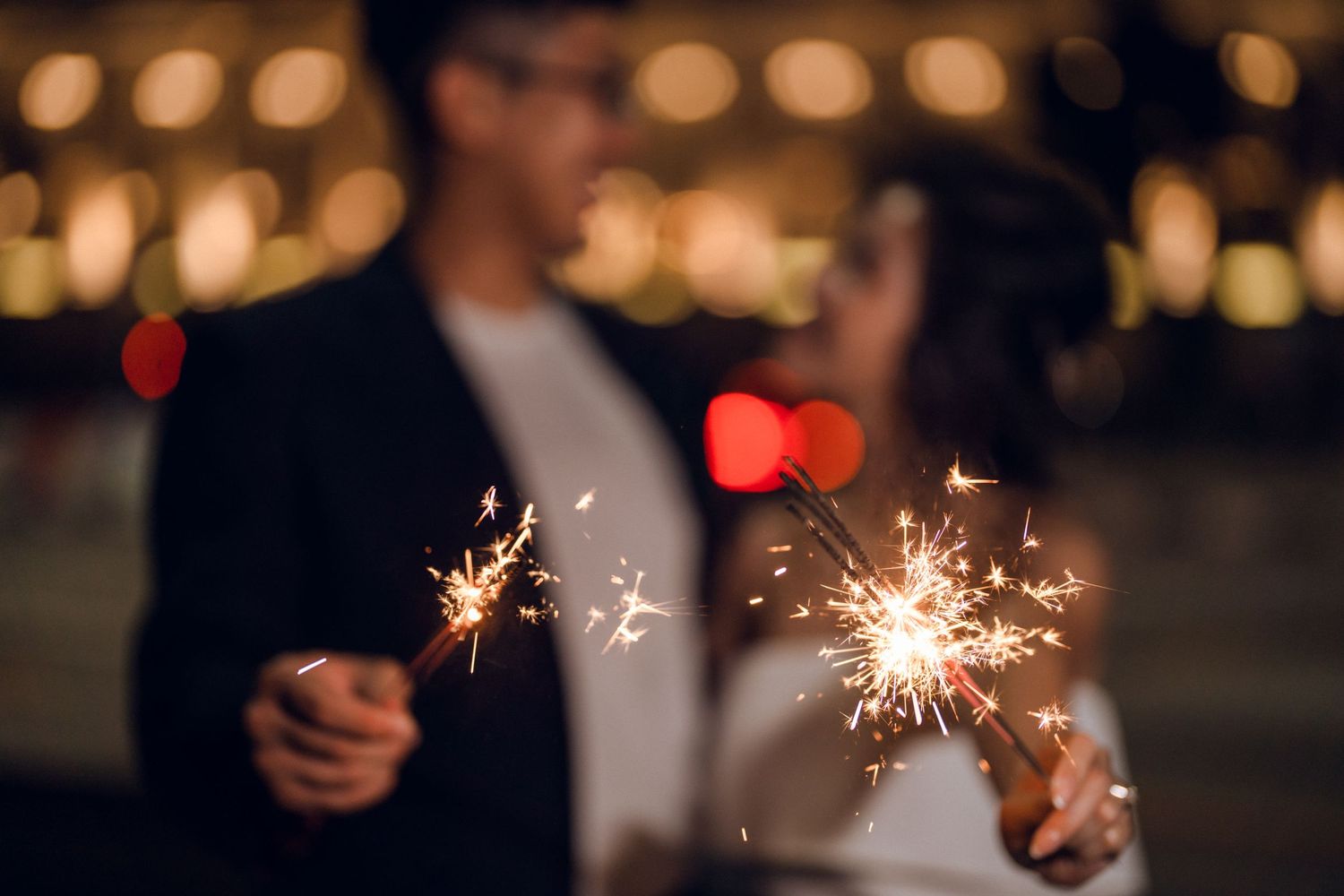 Glowing sparklers illuminate a romantic evening celebration against bokeh lights.