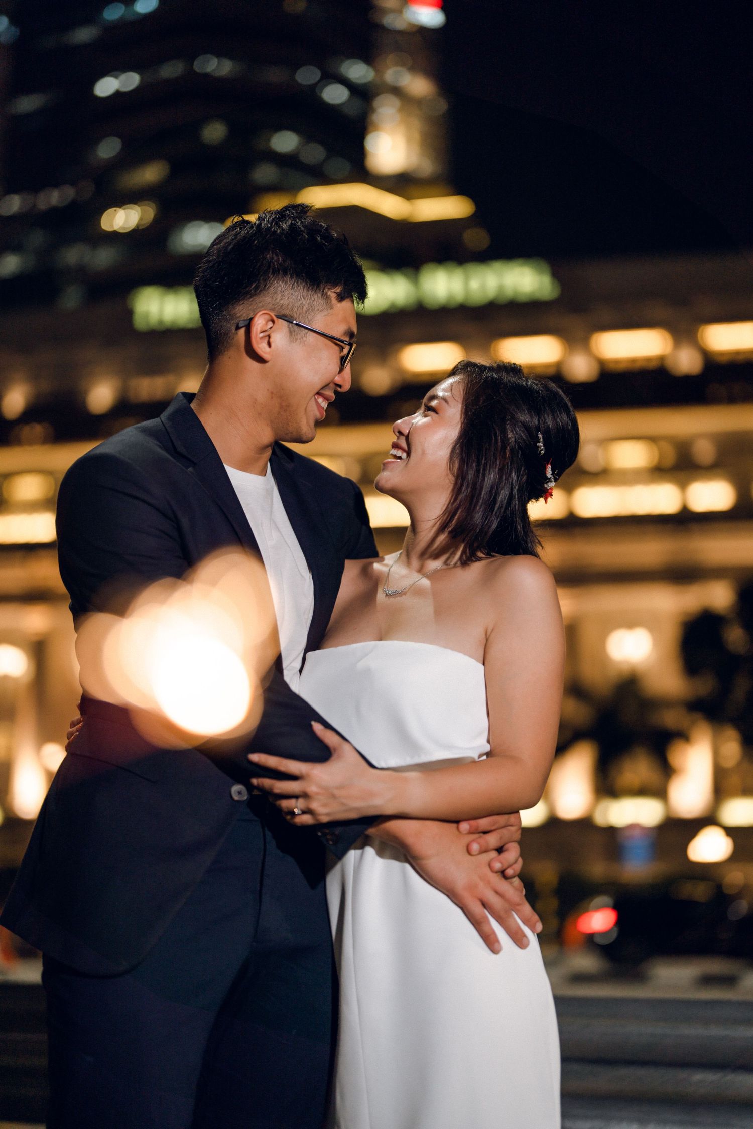 Romantic evening portrait with couple in formal attire against urban backdrop.