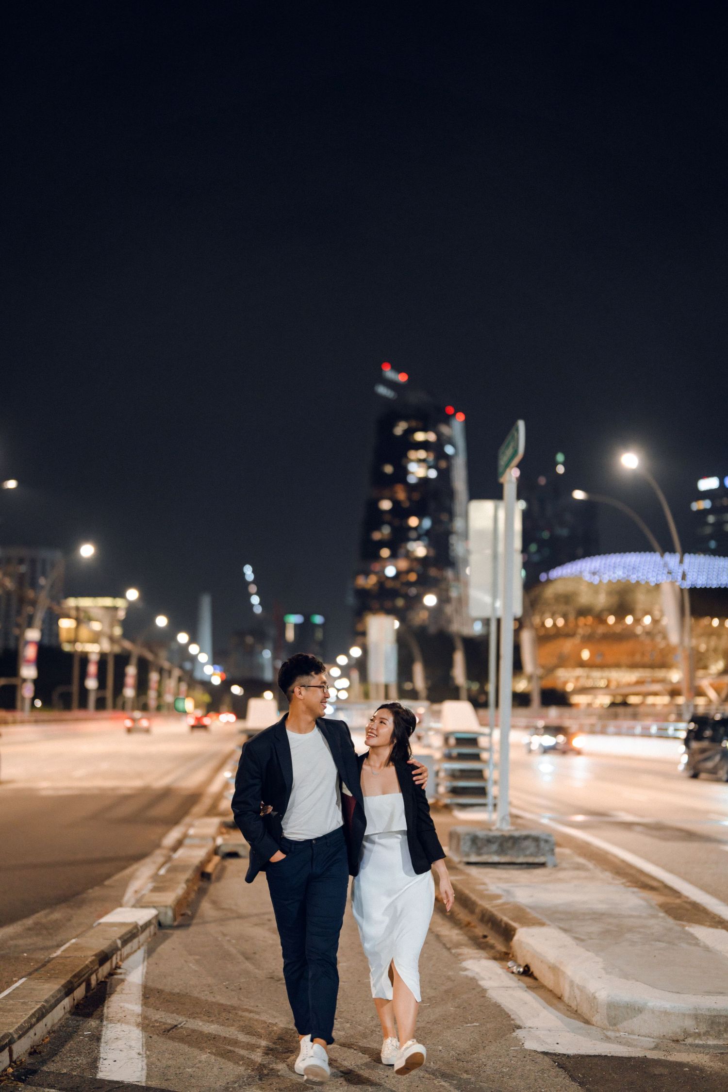 Romantic stroll along urban pathway with city lights and buildings in background.