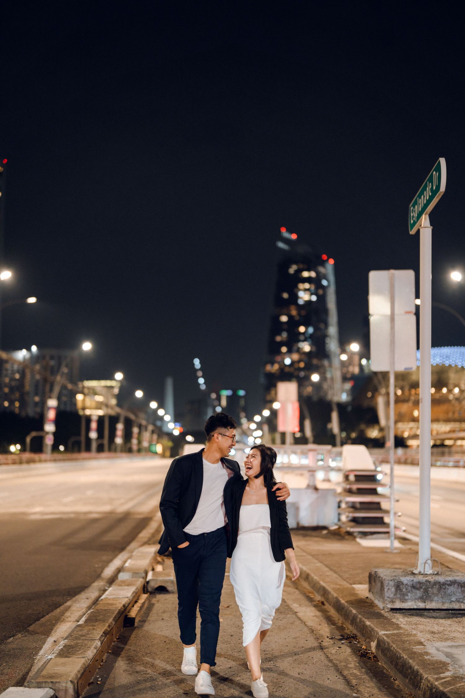 Playful couple moment captured on city street with nighttime skyline.