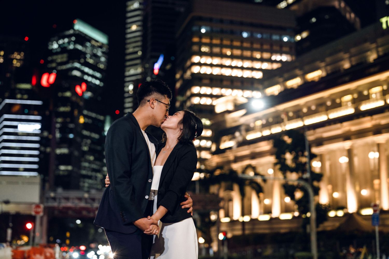 Romantic nighttime photoshoot in front of illuminated city buildings.