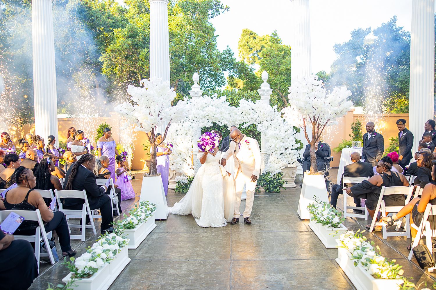 Outdoor wedding ceremony setup with white chairs and floral decorations at sunset.