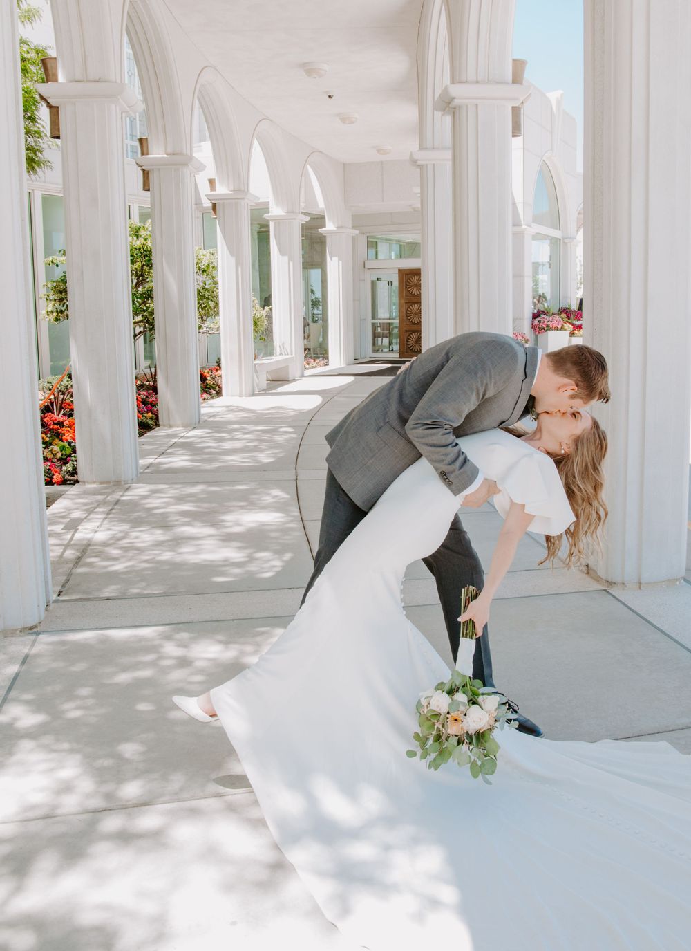 A romantic dip kiss between newlyweds in an elegant white columned walkway.