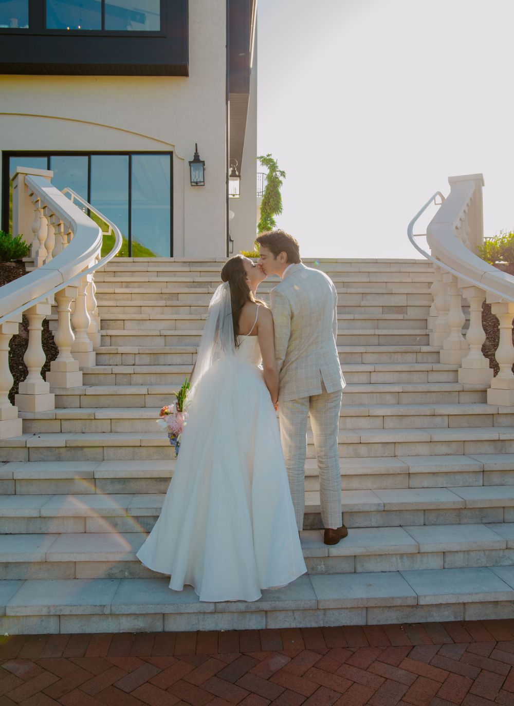Couple descends elegant white stone staircase during formal event.