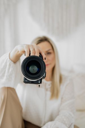 Dina Ozola - female photographer, holding professional camera lens against white background.