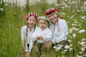 Three people wearing flower crowns sitting in a meadow of white daisies.