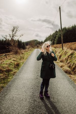 Person in dark coat and nikon camera around standing on a rural road surrounded by countryside landscape in Leitrim, Ireland.