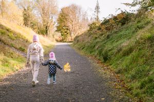 Teenager and toddler walking down a scenic path with small maple Leafe in hand.