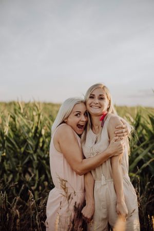 Two people twin sisters, embracing and laughing in a cornfield at sunset.