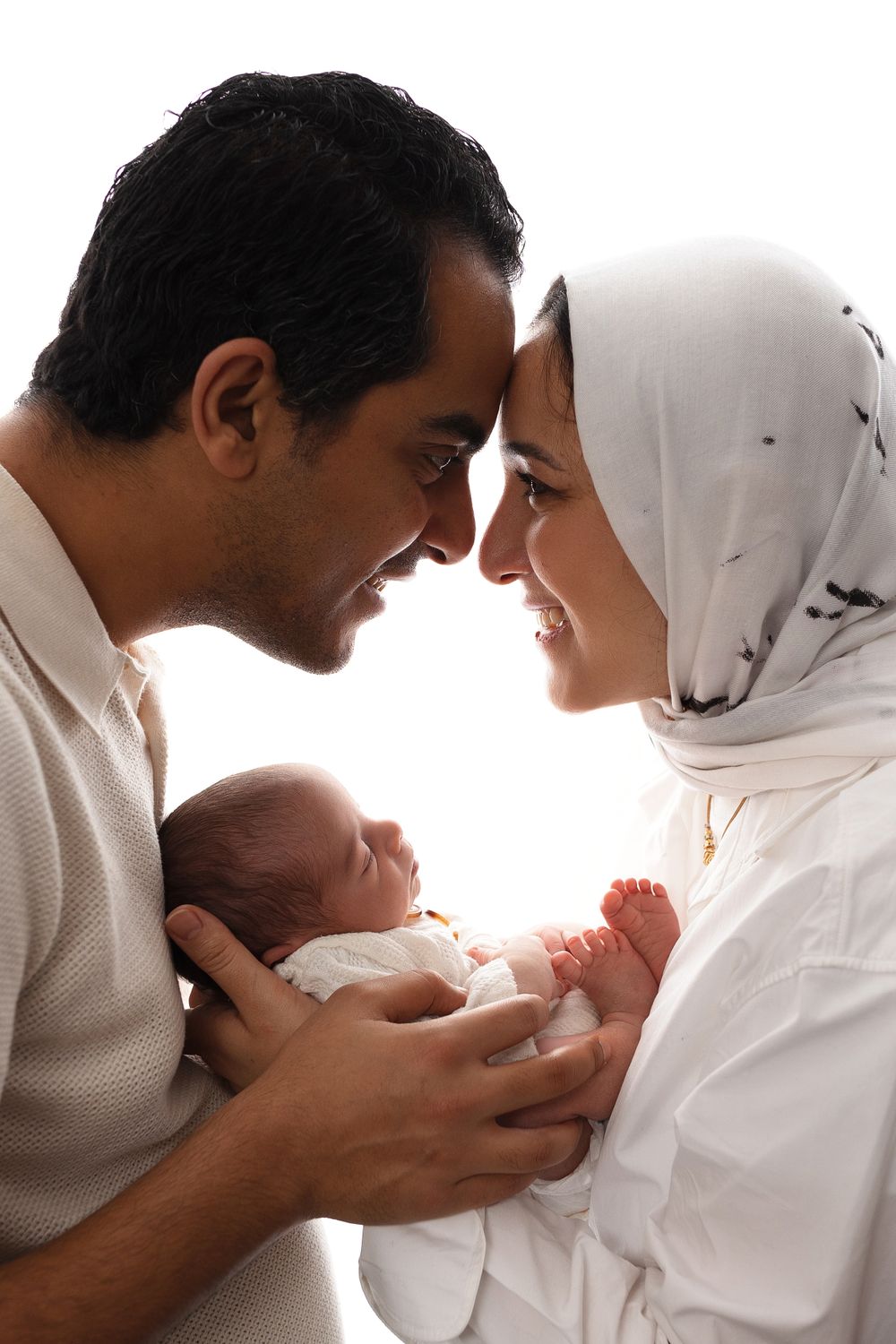 Intimate family portrait showing parents cradling newborn baby against white background.