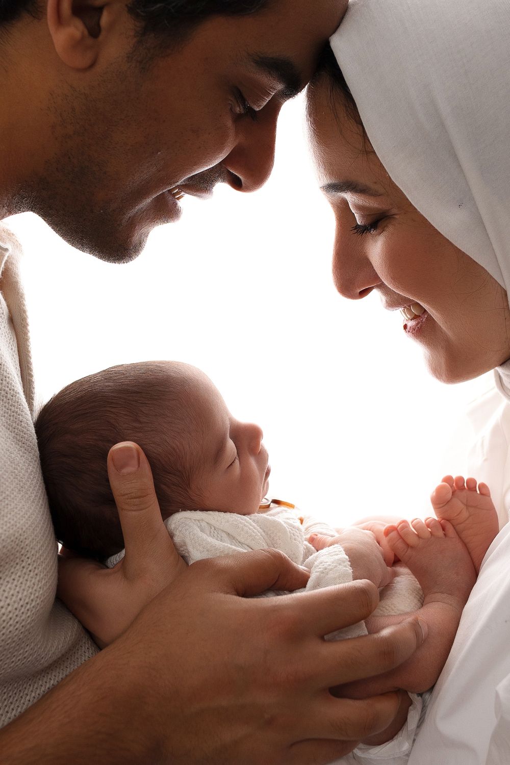 Intimate close-up of parents gazing lovingly at their newborn baby in white.
