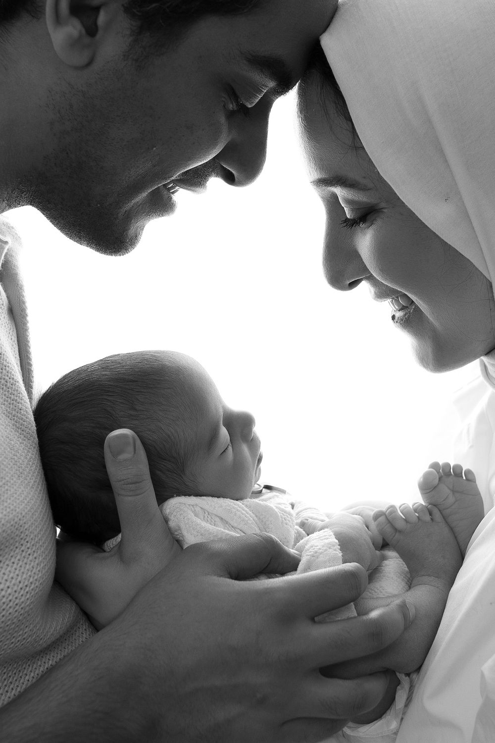 Black and white portrait of parents tenderly holding their newborn baby.