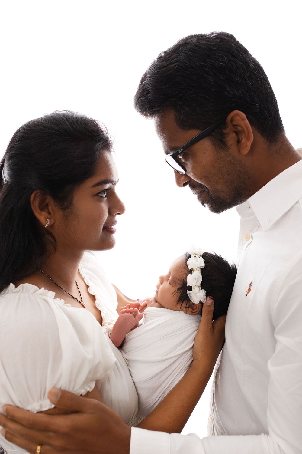 Family portrait against white background with couple holding their newborn baby.