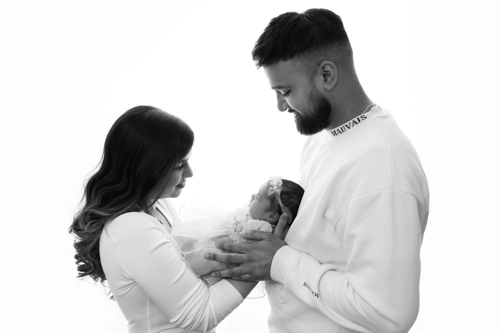 Black and white image of parents gazing lovingly at their swaddled newborn.