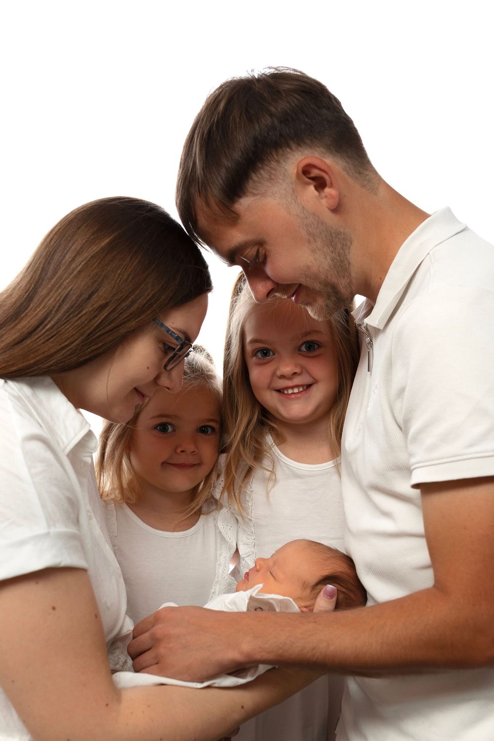 Happy family of four in white shirts smiling at their newborn baby against a white background.
