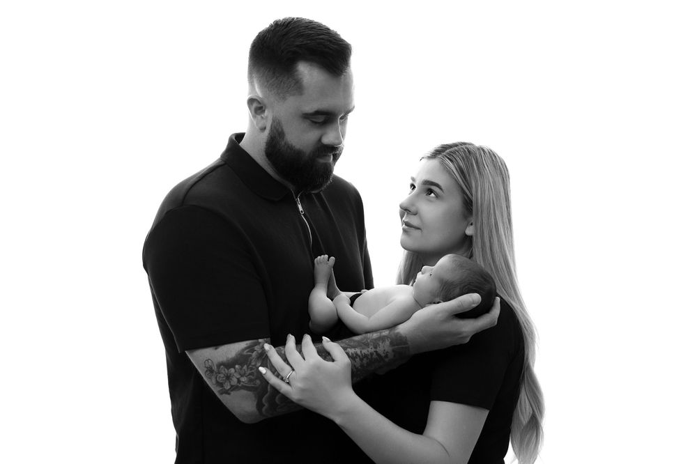 Black and white portrait of a couple in an intimate pose wearing dark clothing against a plain background.