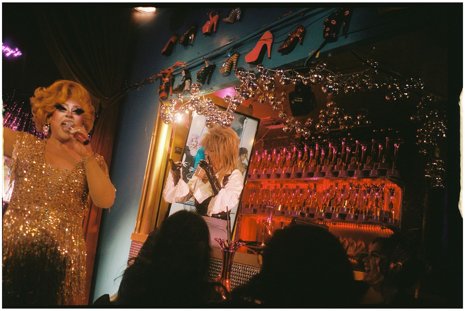 Performers in sparkling costumes entertain on stage at a nightclub with string lights and decorative elements.