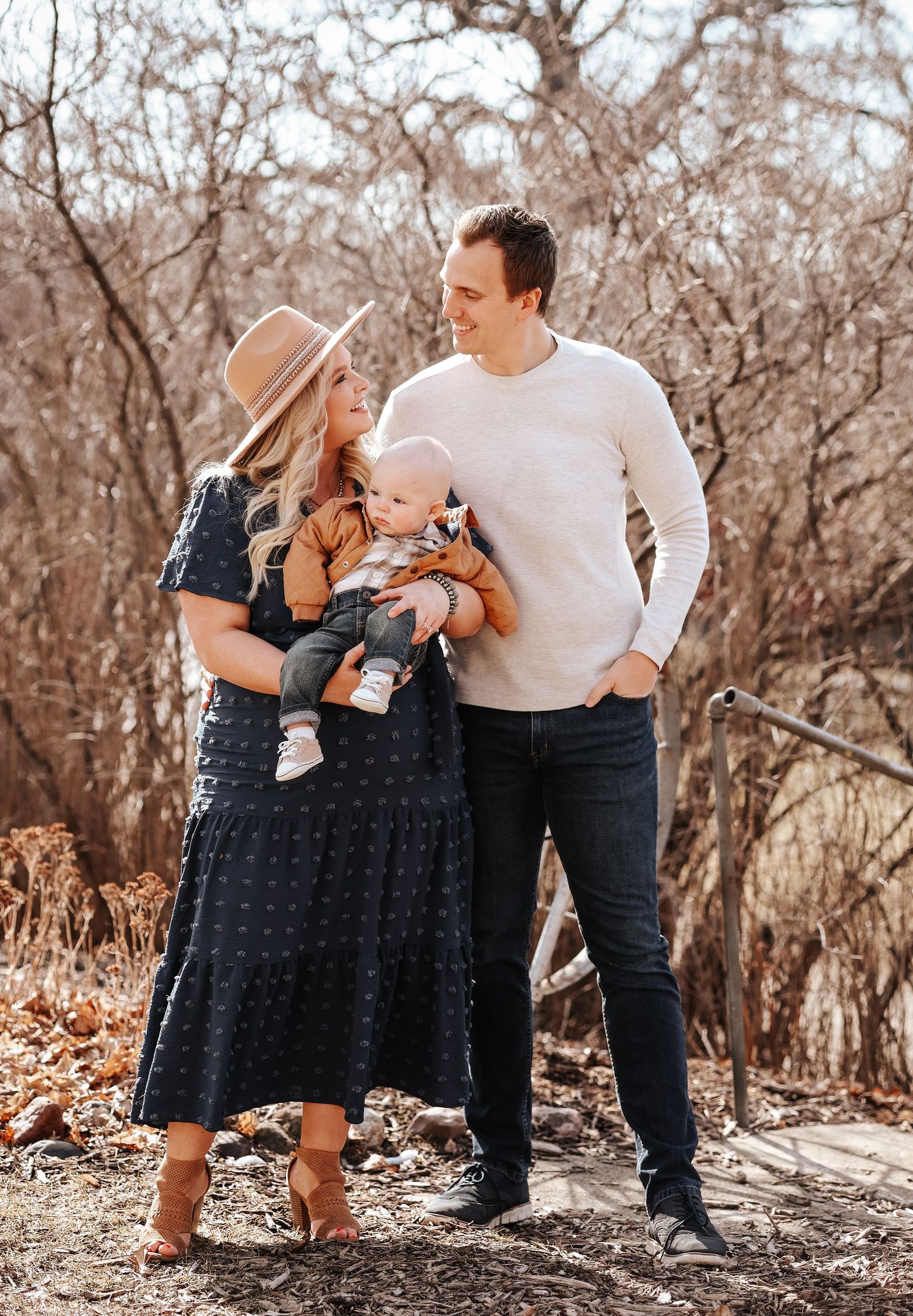 A family in casual attire poses together outdoors during autumn with bare trees in the background.