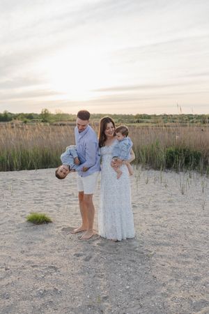 Family in coordinated outfits posing together on sandy beach at sunset with tall grass in background.