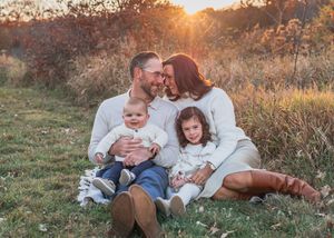 A loving family sits together in a sun-drenched field at golden hour during an autumn evening.