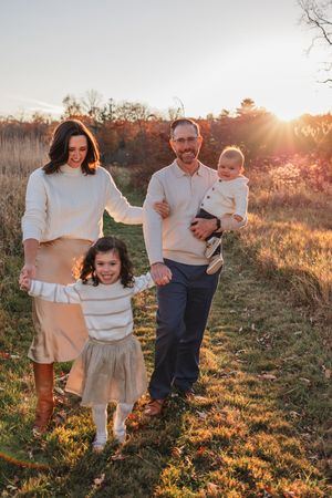 Family of four poses together in a sunlit field at golden hour wearing coordinated cream and beige outfits.