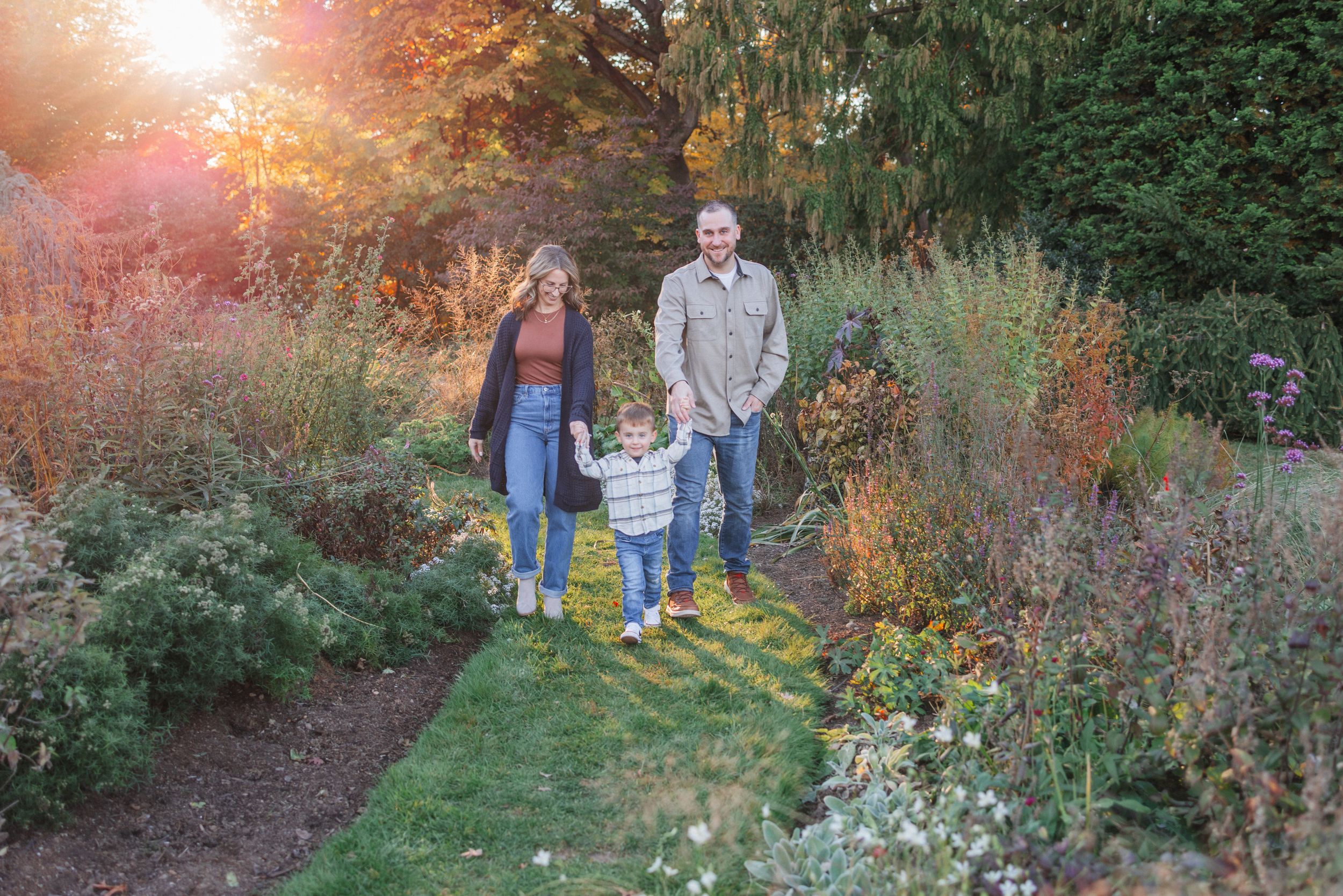 Family enjoying a sunset stroll through a lush garden path surrounded by blooming flowers and greenery.