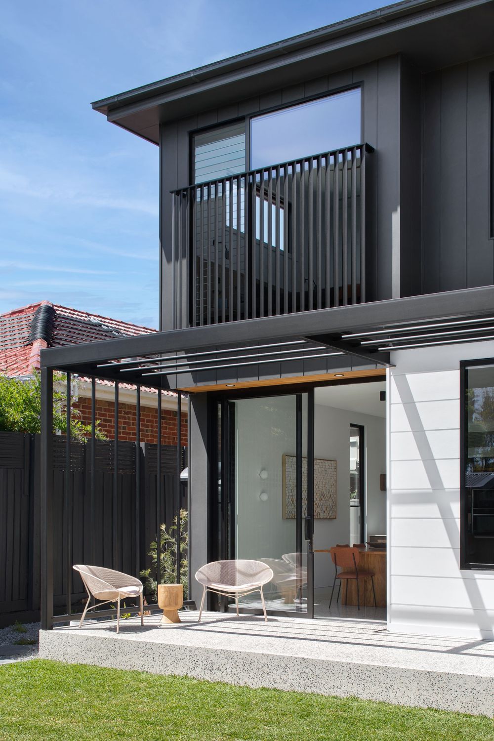 Modern house exterior with black vertical slats and pergola over patio featuring contemporary outdoor seating.