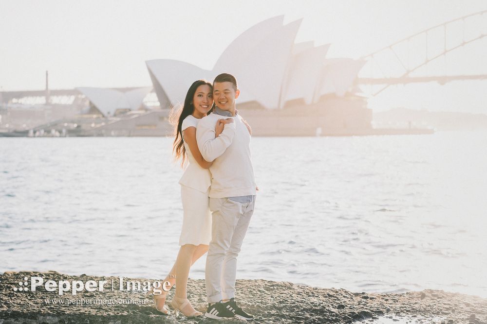 Couple embracing by the waterfront with Sydney Opera House and Harbour Bridge in the background.