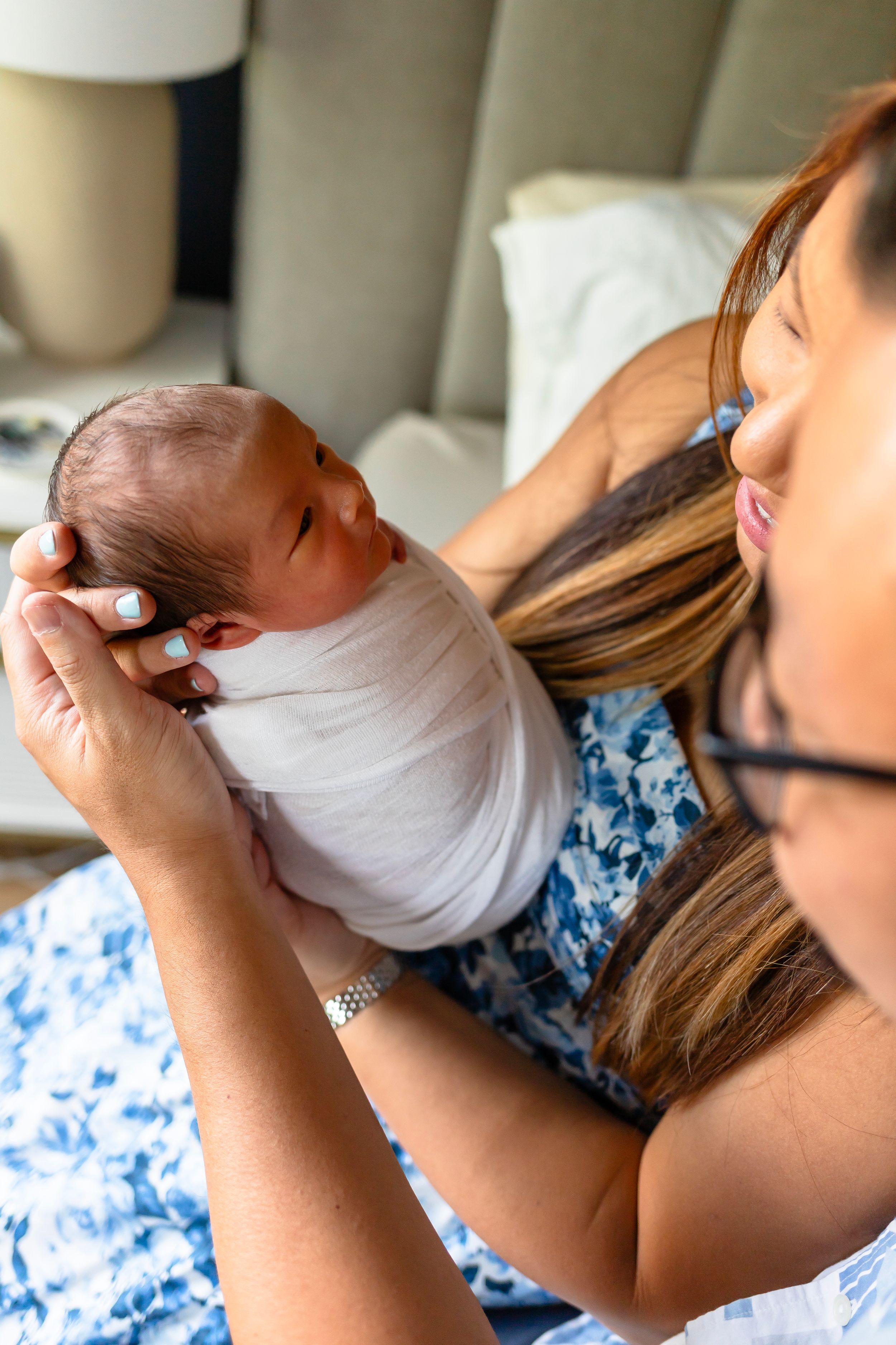 Person in blue floral dress holding newborn baby wrapped in white blanket.