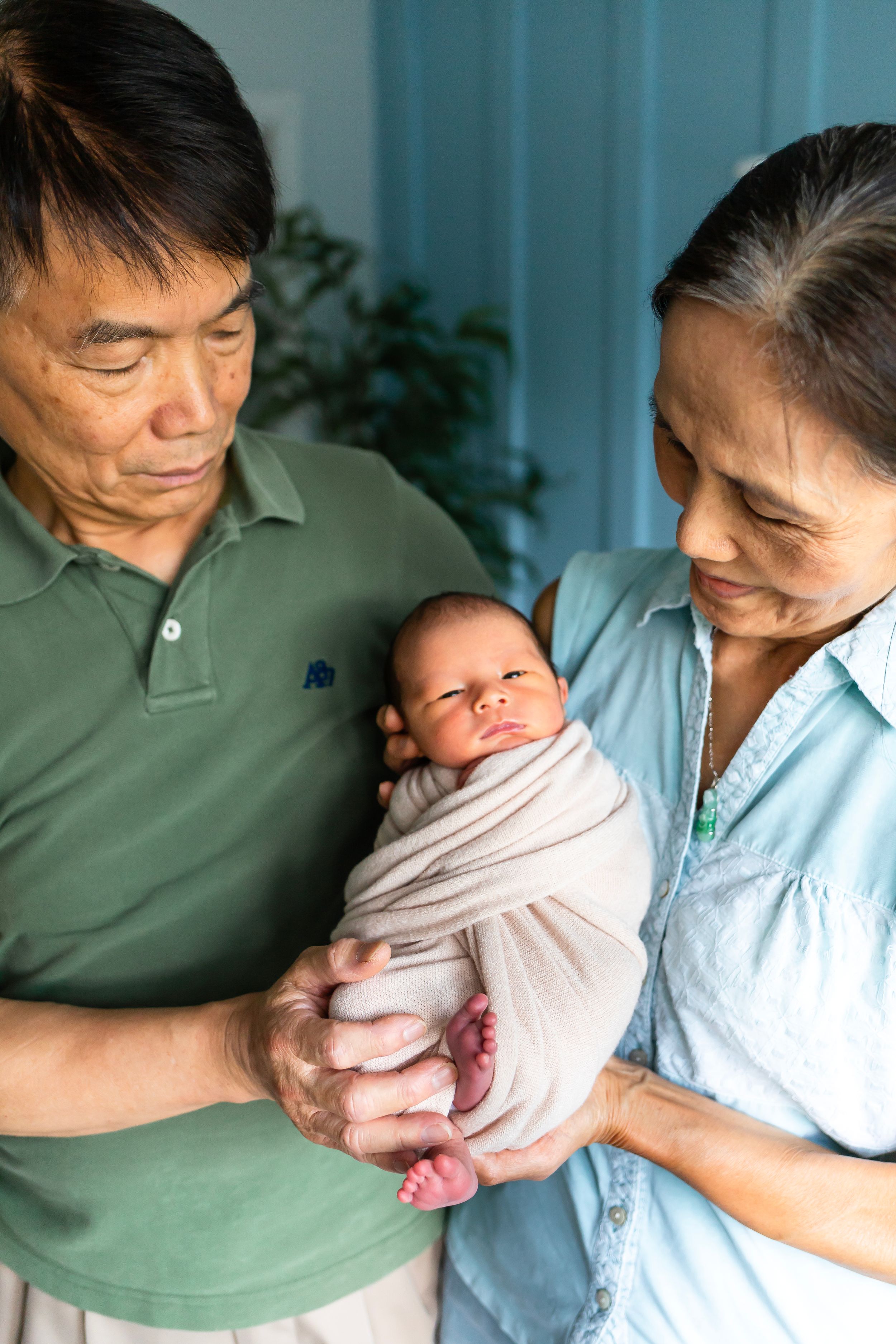 A couple in casual attire tenderly holds their swaddled newborn baby.