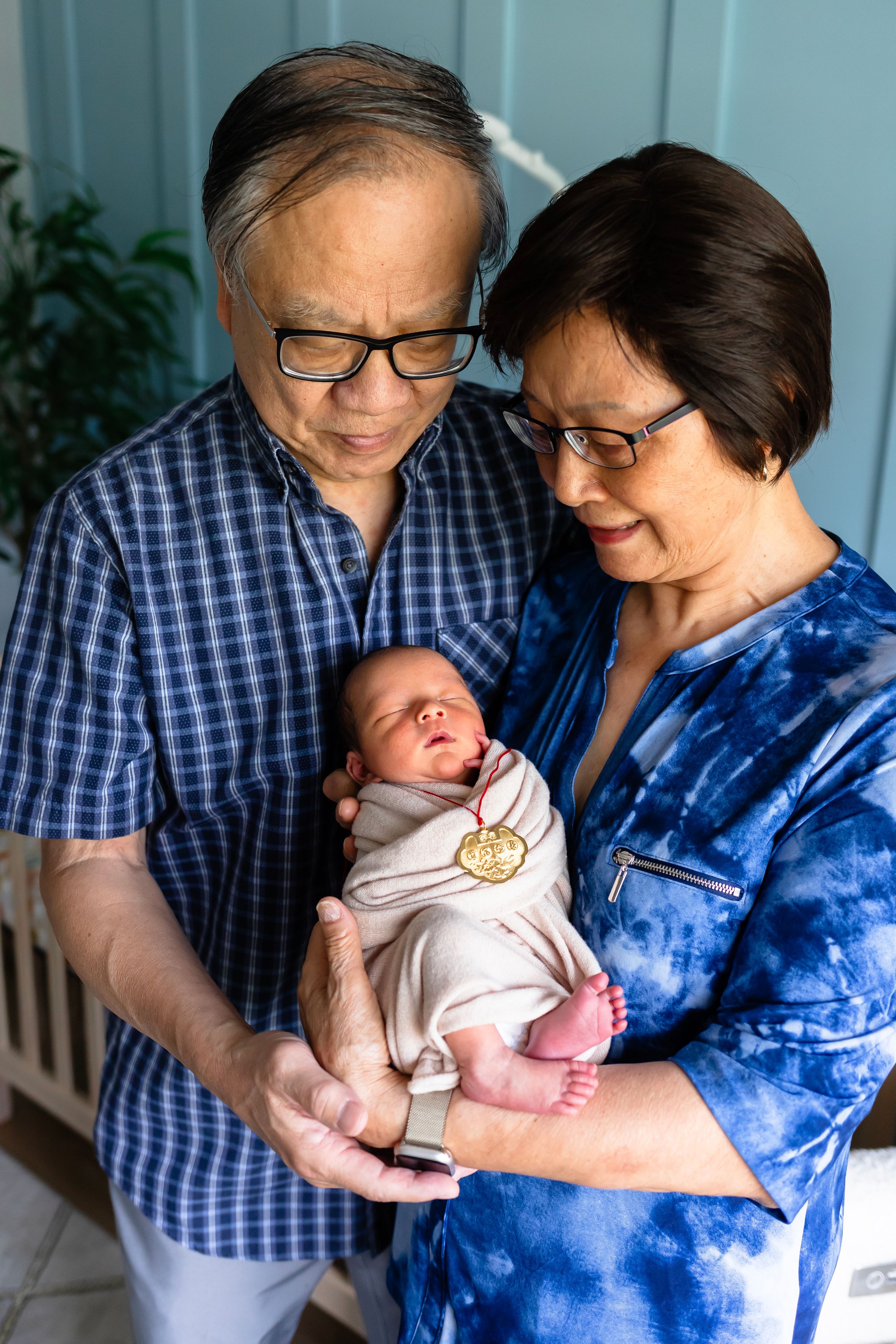 A couple in casual clothing cradles their sleeping newborn baby.