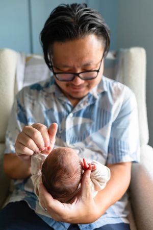 A baby in white swaddle is held and admired in a nursery chair.