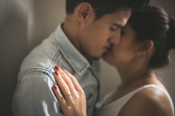 Romantic couple shares intimate almost-kiss moment with woman showing red nails and engagement ring.