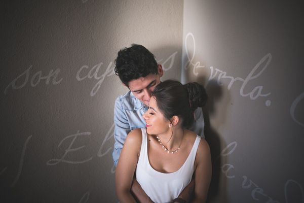 Couple shares tender romantic moment leaning against wall with handwritten text script in soft light.