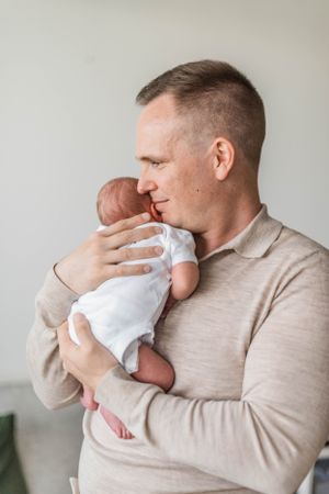 Parent in beige sweater tenderly holding and looking at newborn baby.