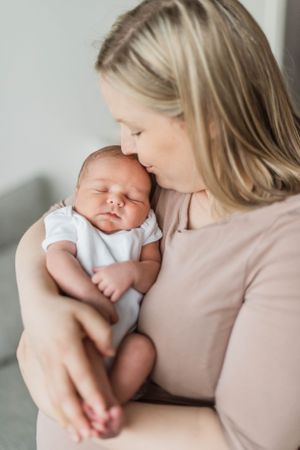 Parent in neutral tones holding sleeping newborn in white onesie.