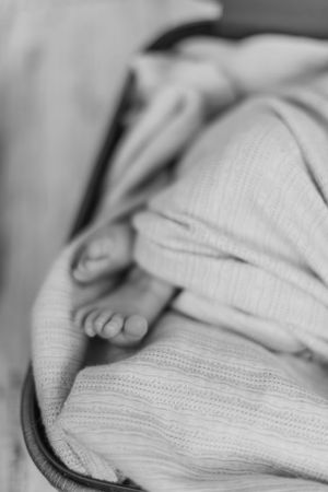 Black and white detail shot of tiny baby feet against textured fabric.