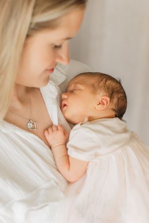 A tender moment between parent and sleeping baby in white clothing against soft white bedding.
