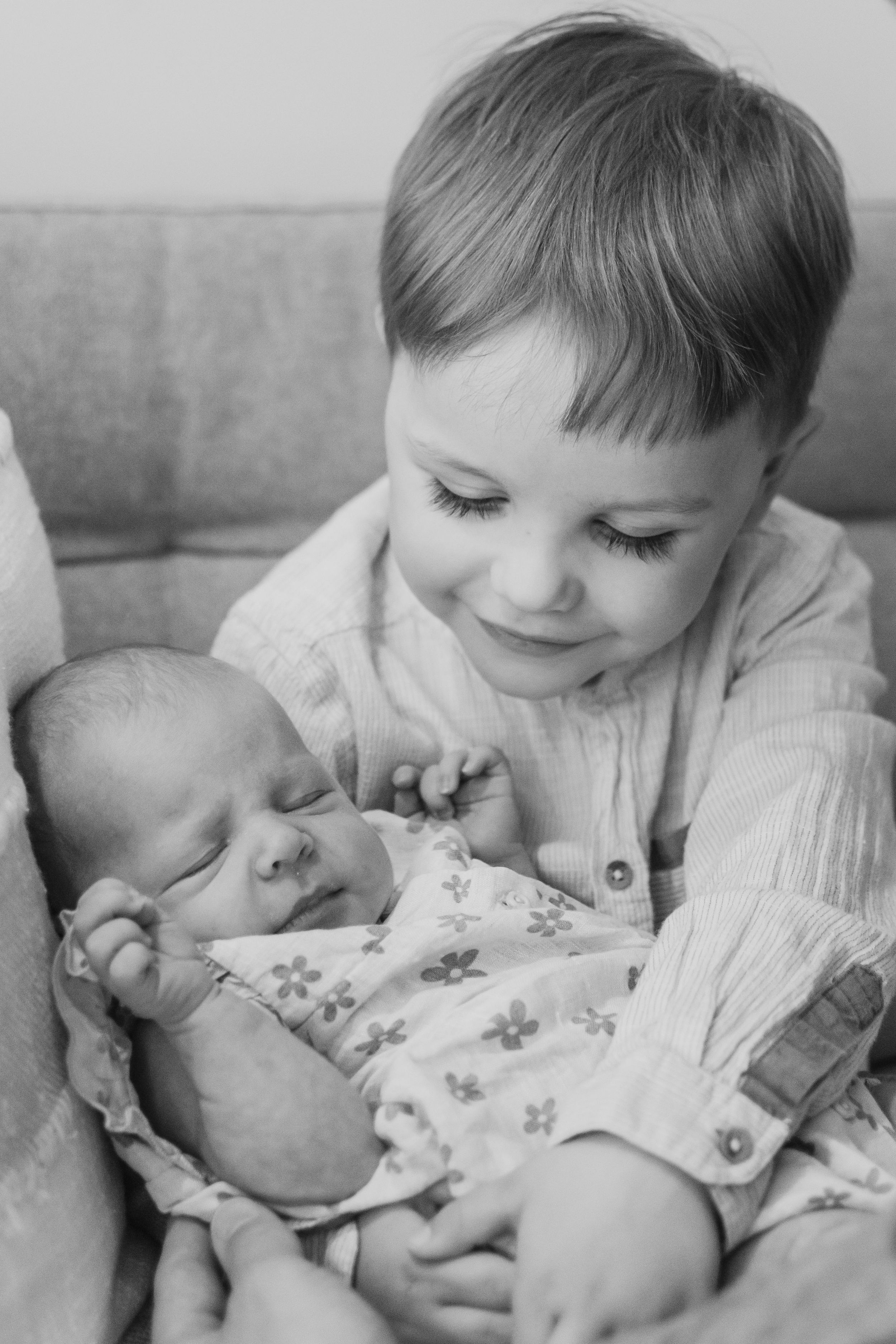 A series of black and white photos showing a young child lovingly gazing at and interacting with a sleeping baby.