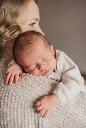 Sleeping newborn baby in white outfit rests peacefully on textured knit blanket in soft neutral tones.