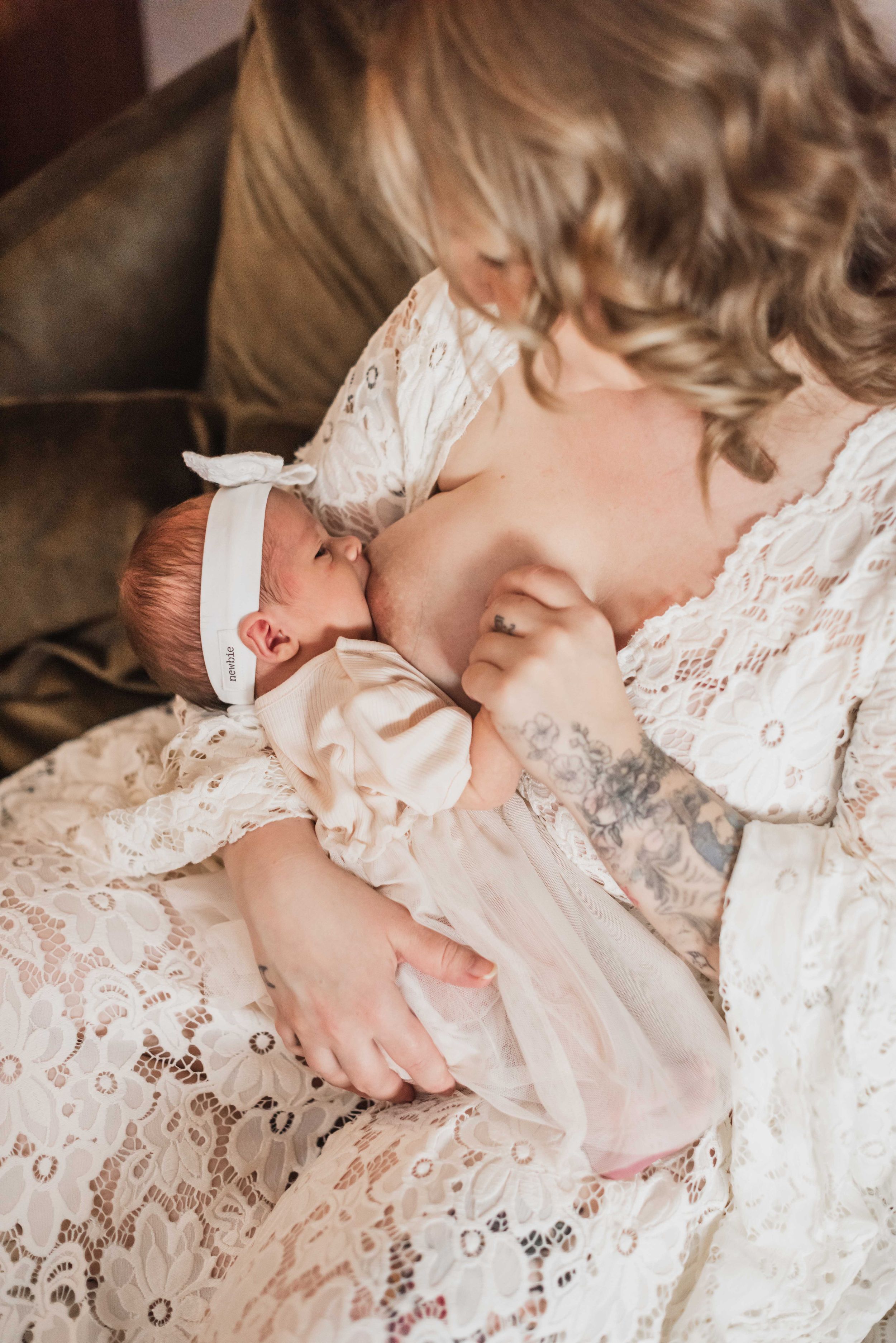 A baby wearing a white lace dress and bow headband sleeps peacefully on delicate lace fabric.