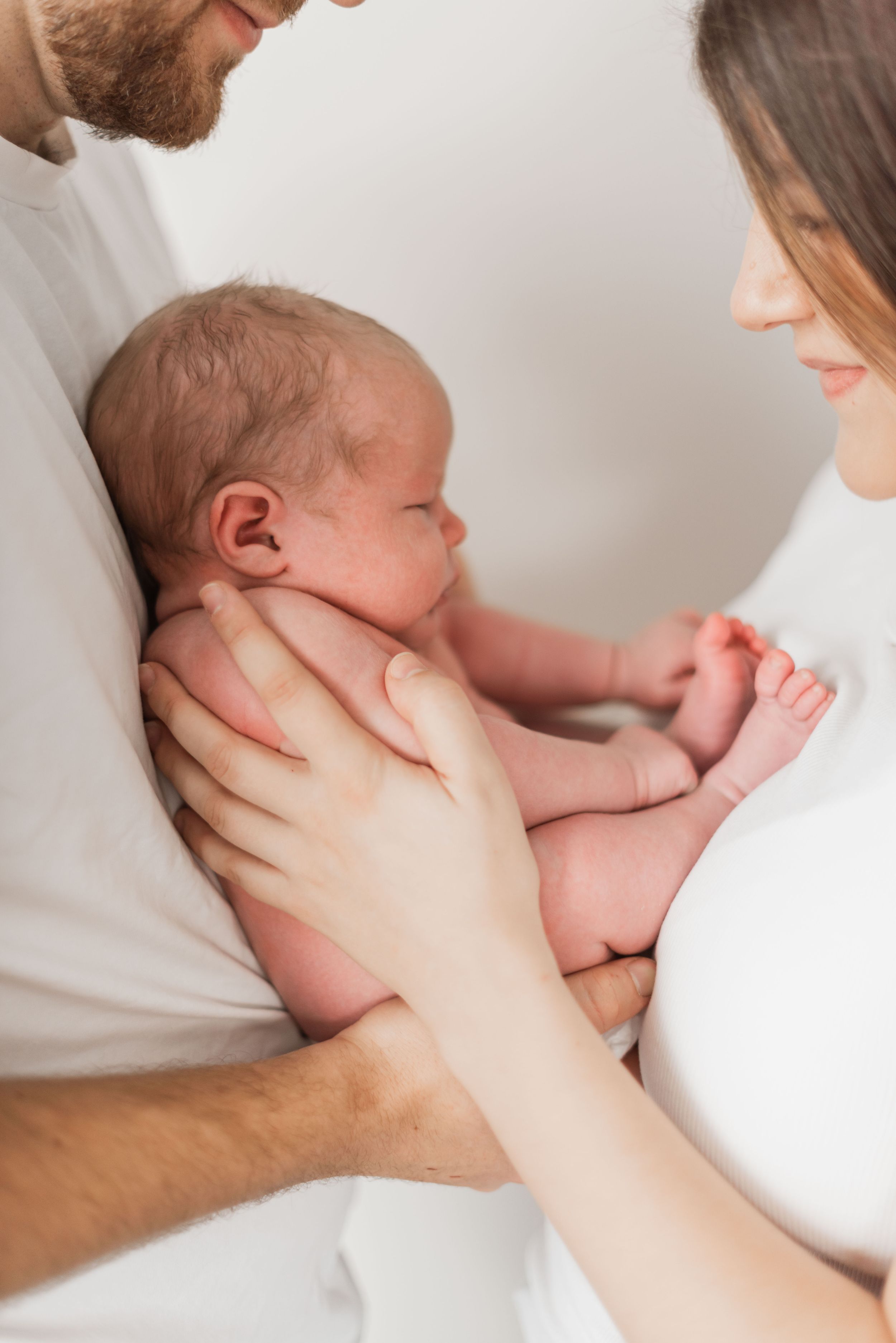 A newborn baby breastfeeding while being supported by gentle hands in a soft, natural light setting.