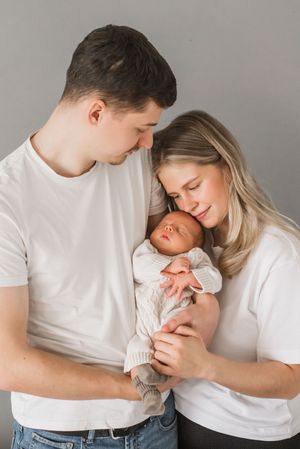 A series of intimate family portraits showing tender moments between parents and their newborn baby in white clothing.