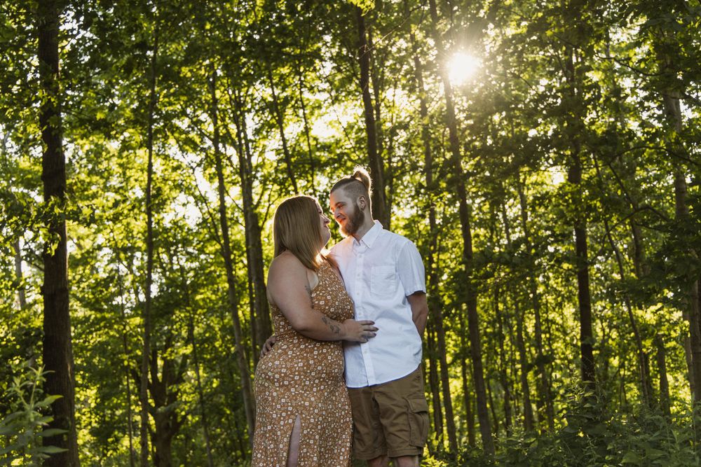 A couple shares an intimate moment in sunlit woods during golden hour.